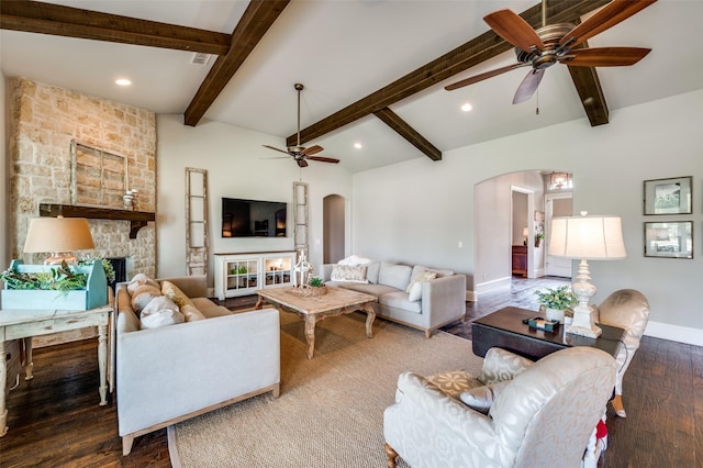 living room with dark wood-type flooring, ceiling fan, a fireplace, and vaulted ceiling with beams