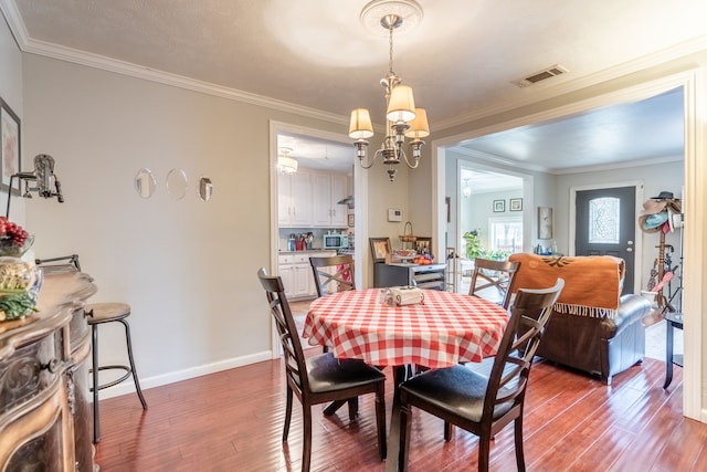 dining space featuring dark hardwood / wood-style flooring, ornamental molding, and a chandelier