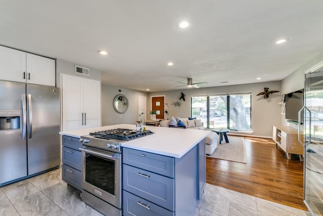 kitchen with appliances with stainless steel finishes, blue cabinets, white cabinetry, a center island, and ceiling fan