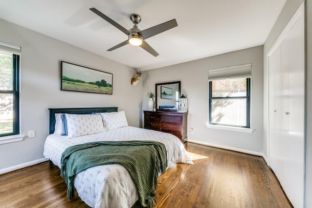 bedroom with multiple windows, dark wood-type flooring, ceiling fan, and a closet