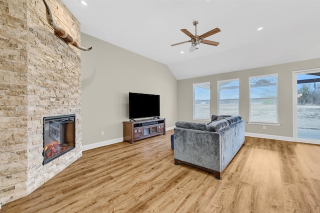 living room with vaulted ceiling, a stone fireplace, ceiling fan, and light wood-type flooring