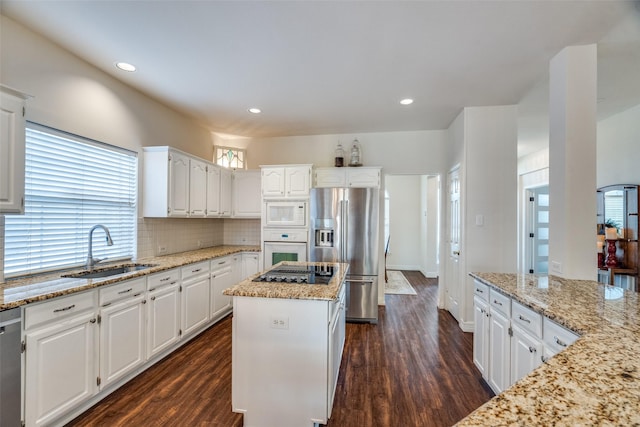 kitchen with sink, appliances with stainless steel finishes, a center island, light stone counters, and white cabinets