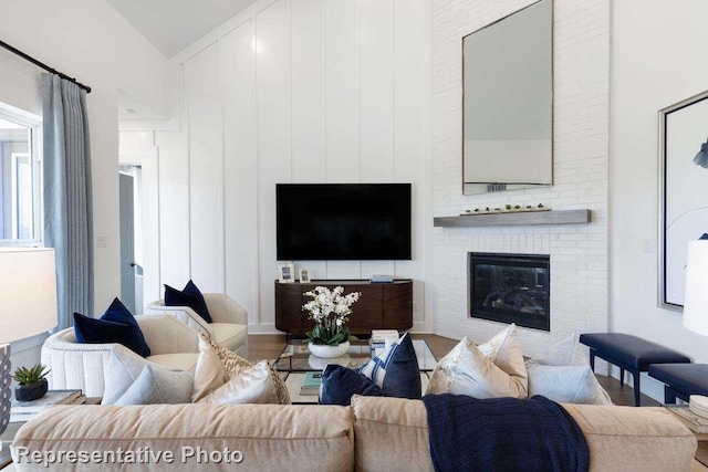 living room with hardwood / wood-style flooring, vaulted ceiling, and a brick fireplace