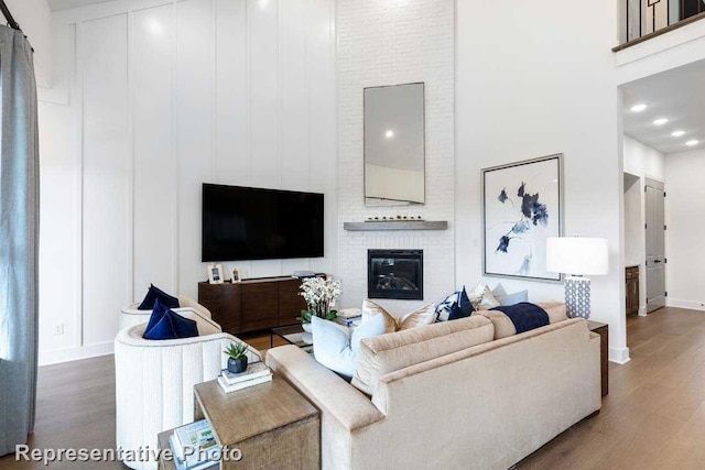 living room featuring dark wood-type flooring, a towering ceiling, and a brick fireplace