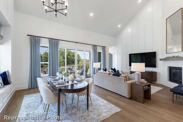 living room with an inviting chandelier, light hardwood / wood-style flooring, high vaulted ceiling, and a large fireplace