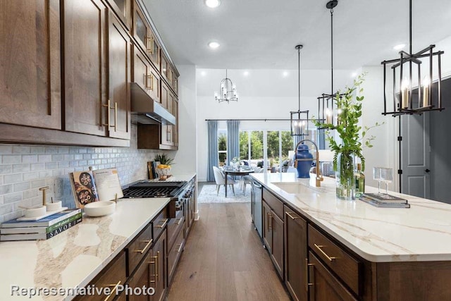 kitchen with light stone countertops, sink, light wood-type flooring, and decorative light fixtures