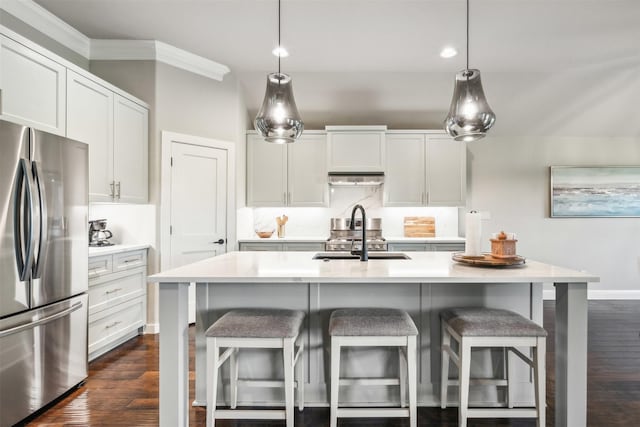 kitchen featuring sink, appliances with stainless steel finishes, a kitchen island with sink, white cabinets, and decorative light fixtures