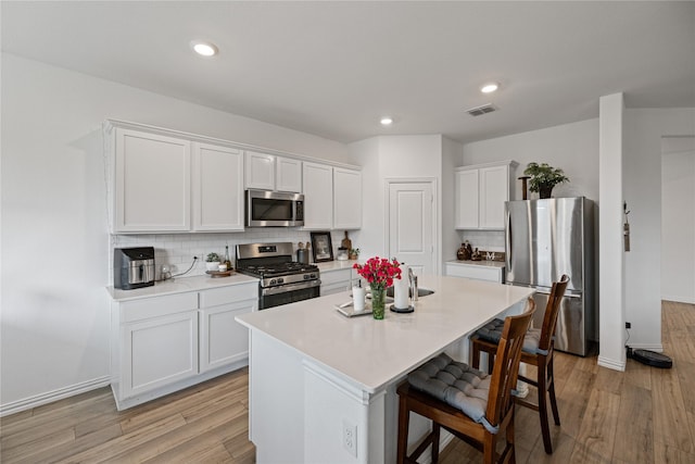 kitchen featuring a breakfast bar, white cabinetry, stainless steel appliances, a center island with sink, and light wood-type flooring