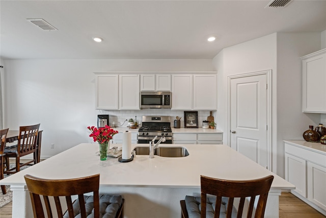 kitchen featuring sink, appliances with stainless steel finishes, white cabinets, a kitchen island with sink, and backsplash