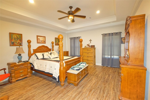 bedroom featuring ceiling fan, ornamental molding, a tray ceiling, and light hardwood / wood-style floors