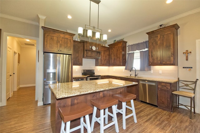 kitchen with a kitchen island, a breakfast bar, sink, light stone counters, and stainless steel appliances