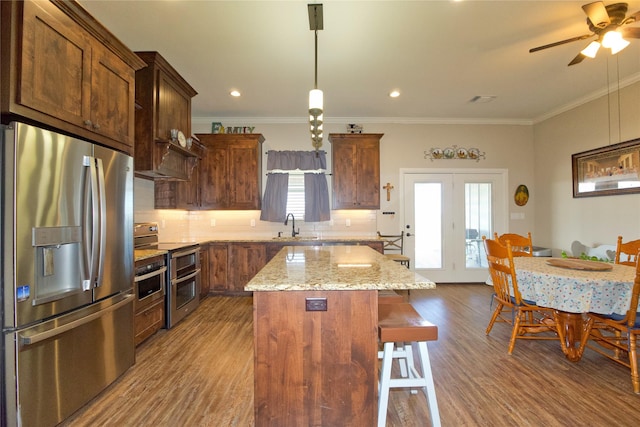 kitchen featuring a kitchen island, sink, hanging light fixtures, light stone counters, and stainless steel appliances