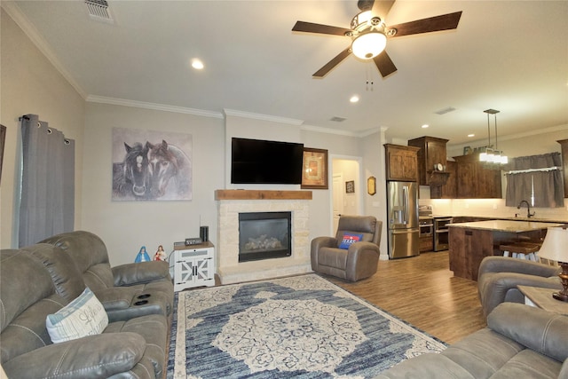 living room featuring crown molding, ceiling fan, a stone fireplace, and light hardwood / wood-style flooring