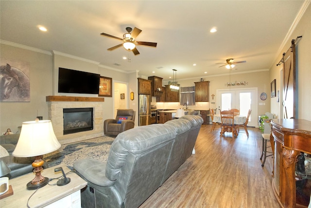 living room featuring sink, crown molding, ceiling fan, a barn door, and light wood-type flooring