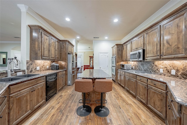 kitchen with sink, a kitchen breakfast bar, a center island, stainless steel appliances, and light stone countertops