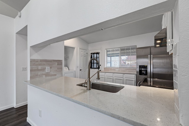 kitchen featuring washer / dryer, sink, light stone counters, stainless steel fridge, and kitchen peninsula