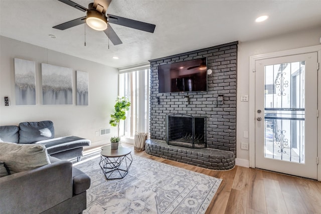 living room featuring ceiling fan, wood-type flooring, a brick fireplace, and a textured ceiling