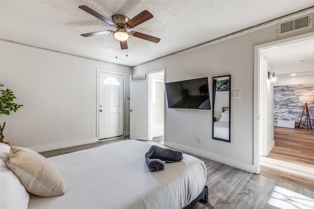 bedroom with ceiling fan, ensuite bath, light hardwood / wood-style floors, and a textured ceiling