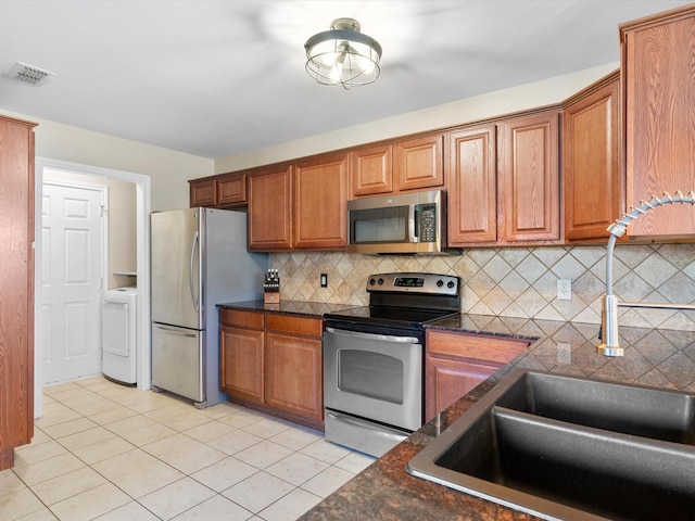 kitchen with light tile patterned flooring, washer / dryer, sink, tasteful backsplash, and stainless steel appliances