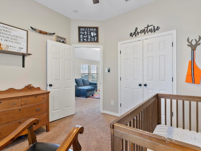 bedroom with a nursery area, light colored carpet, ceiling fan, and a closet