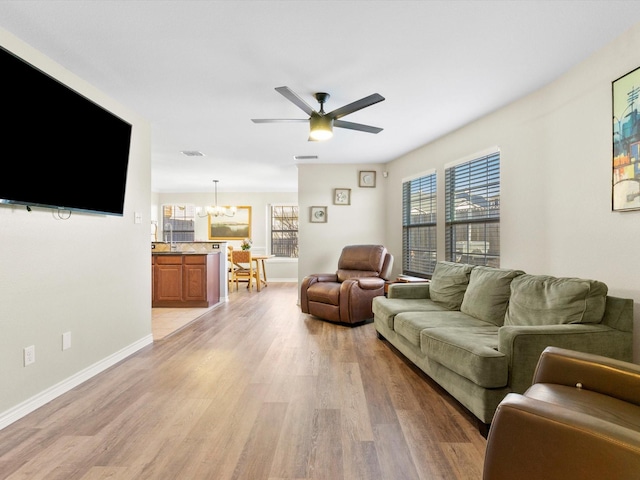 living room featuring plenty of natural light, ceiling fan with notable chandelier, and light hardwood / wood-style flooring