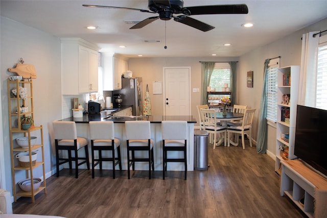 kitchen featuring dark hardwood / wood-style floors, stainless steel refrigerator, white cabinetry, a kitchen breakfast bar, and kitchen peninsula