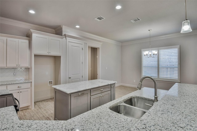 kitchen with white cabinetry, light stone counters, sink, and hanging light fixtures