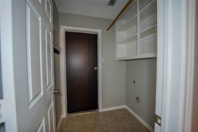 clothes washing area with electric dryer hookup, a textured ceiling, and light tile patterned floors