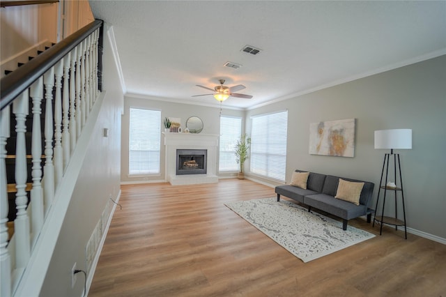 living room featuring hardwood / wood-style flooring, crown molding, ceiling fan, and a fireplace