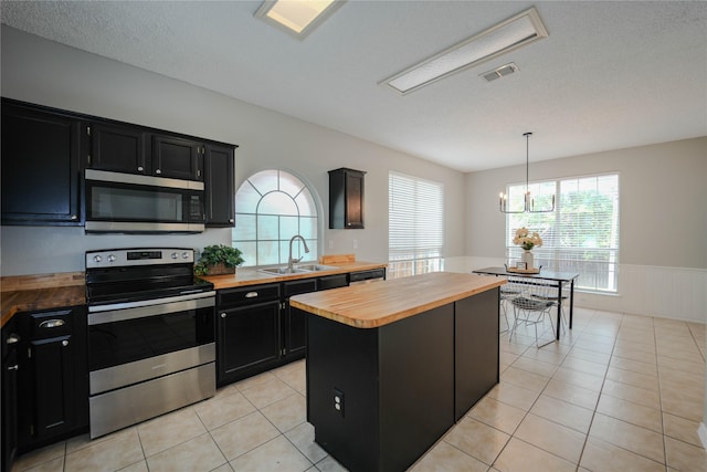 kitchen featuring pendant lighting, butcher block countertops, sink, stainless steel appliances, and a kitchen island