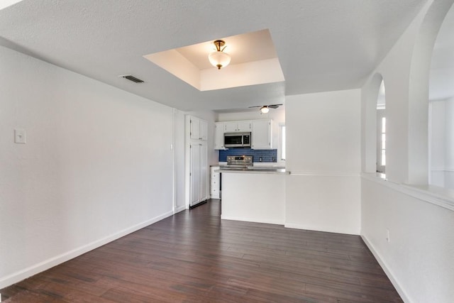 unfurnished living room featuring a raised ceiling, ceiling fan, dark hardwood / wood-style floors, and a textured ceiling