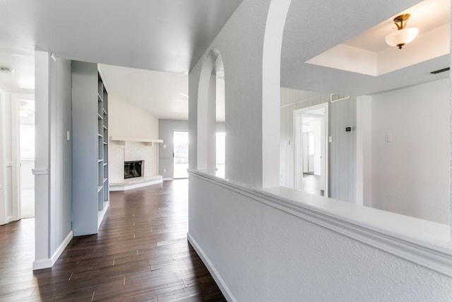 hallway featuring baseboards, visible vents, arched walkways, dark wood-style flooring, and a tray ceiling