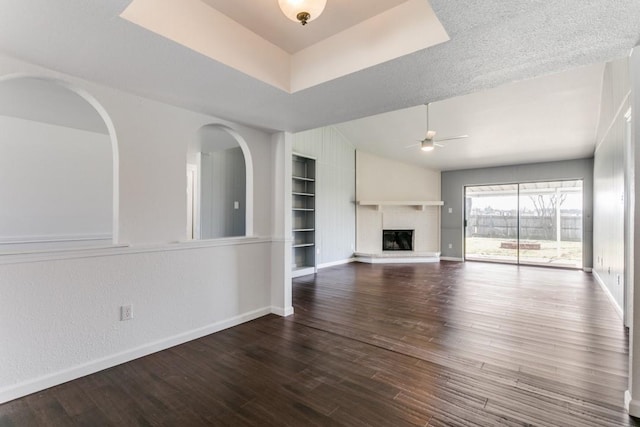 unfurnished living room with built in shelves, ceiling fan, wood-type flooring, and a fireplace