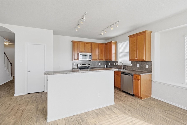 kitchen featuring appliances with stainless steel finishes, a center island, decorative backsplash, and light hardwood / wood-style flooring