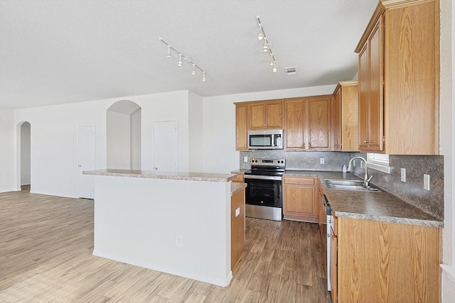 kitchen featuring appliances with stainless steel finishes, sink, decorative backsplash, a center island, and light wood-type flooring