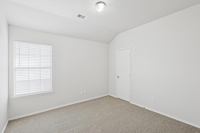 spare room featuring vaulted ceiling, carpet floors, and a textured ceiling