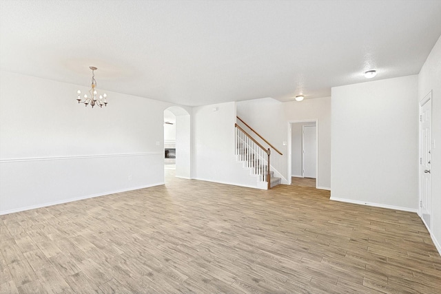 unfurnished living room with a textured ceiling, an inviting chandelier, and light hardwood / wood-style flooring