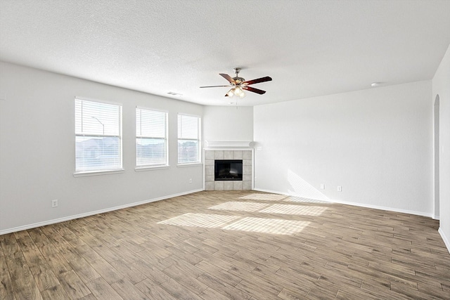 unfurnished living room featuring ceiling fan, a tiled fireplace, light hardwood / wood-style flooring, and a textured ceiling