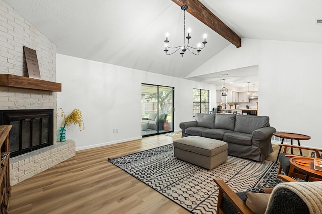 living room with hardwood / wood-style flooring, a brick fireplace, vaulted ceiling with beams, and an inviting chandelier