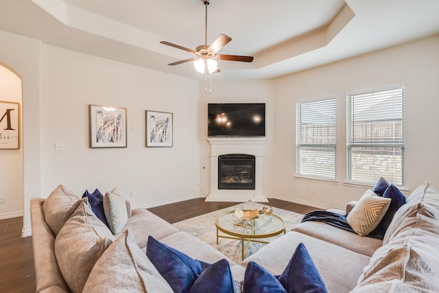 living room featuring ceiling fan, dark hardwood / wood-style flooring, and a tray ceiling