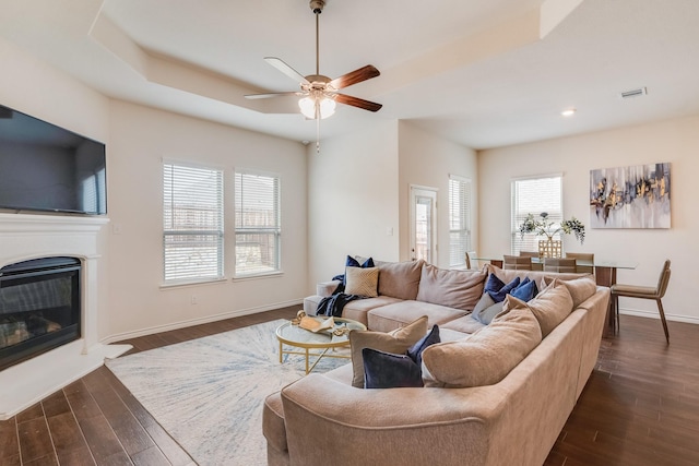 living room with ceiling fan, dark hardwood / wood-style floors, and a raised ceiling