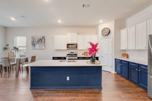 kitchen featuring blue cabinetry, sink, appliances with stainless steel finishes, a kitchen island with sink, and white cabinets