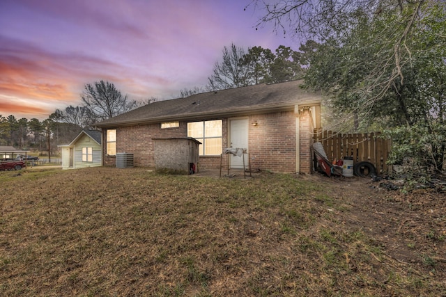 back house at dusk featuring cooling unit and a yard