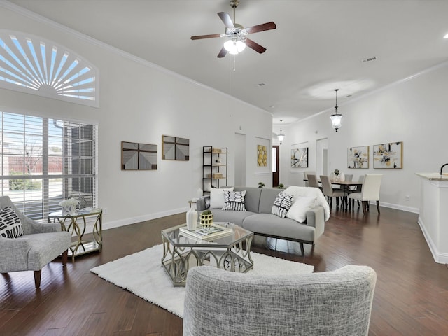 living room featuring a high ceiling, ornamental molding, dark wood-type flooring, and ceiling fan