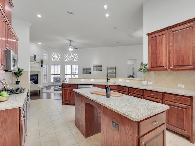 kitchen featuring appliances with stainless steel finishes, backsplash, a center island, light stone counters, and kitchen peninsula