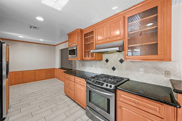 kitchen with appliances with stainless steel finishes, tasteful backsplash, ornamental molding, dark stone counters, and light wood-type flooring