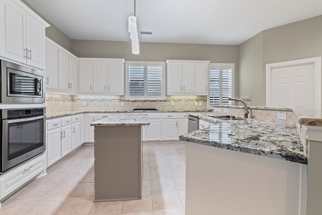 kitchen with sink, appliances with stainless steel finishes, hanging light fixtures, a center island, and white cabinets