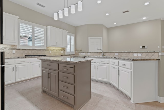 kitchen featuring gray cabinetry, white cabinetry, light stone counters, hanging light fixtures, and a kitchen island