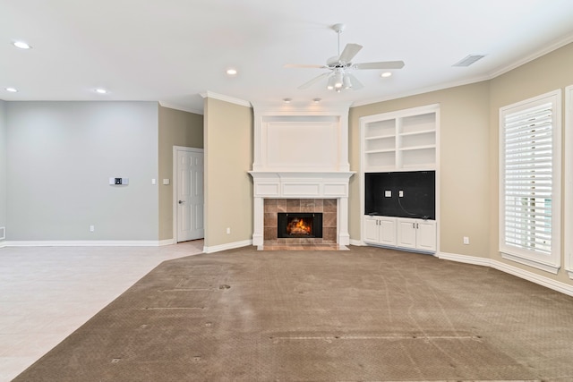 unfurnished living room featuring crown molding, built in features, a tile fireplace, ceiling fan, and light carpet