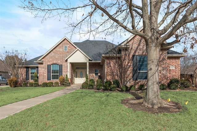 view of front of house with roof with shingles, fence, a front lawn, and brick siding